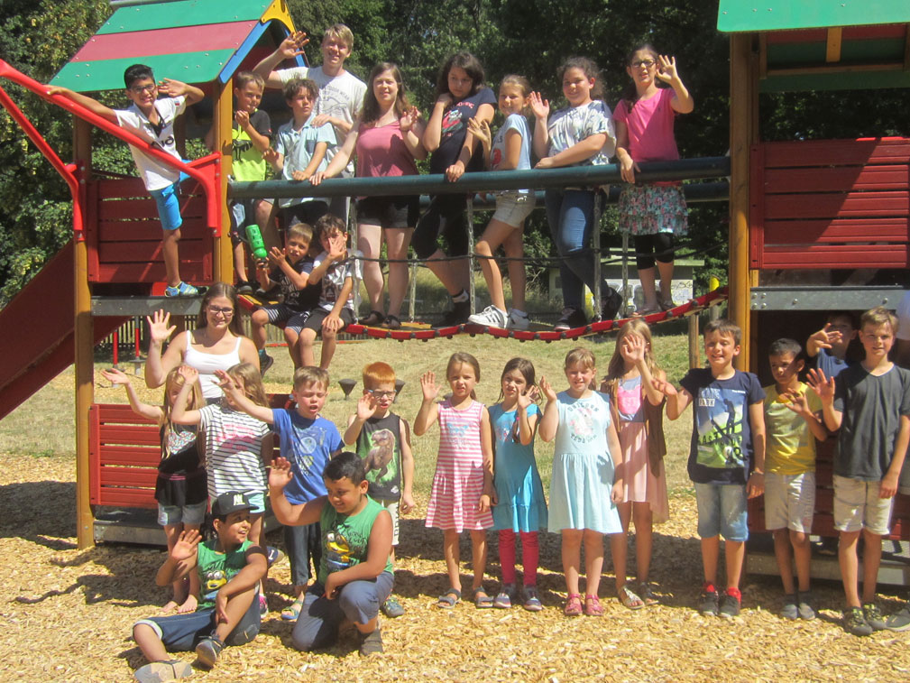 Kinder und Jugendliche winken auf und vor einem Spielgerät.