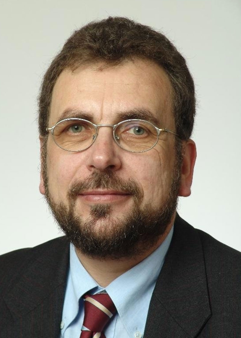 Professionelles Porträt eines bärtigen Mannes mit Brille.