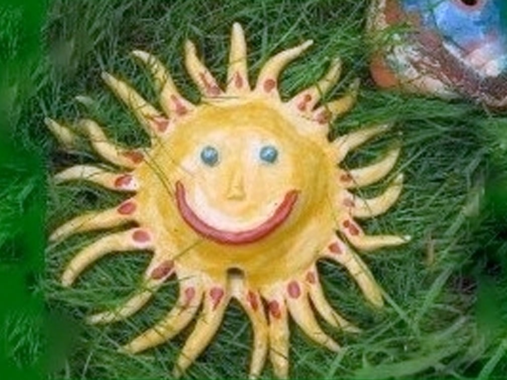 Keramik-Sonnendekoration mit lächelndem Gesicht im grünen Gras.