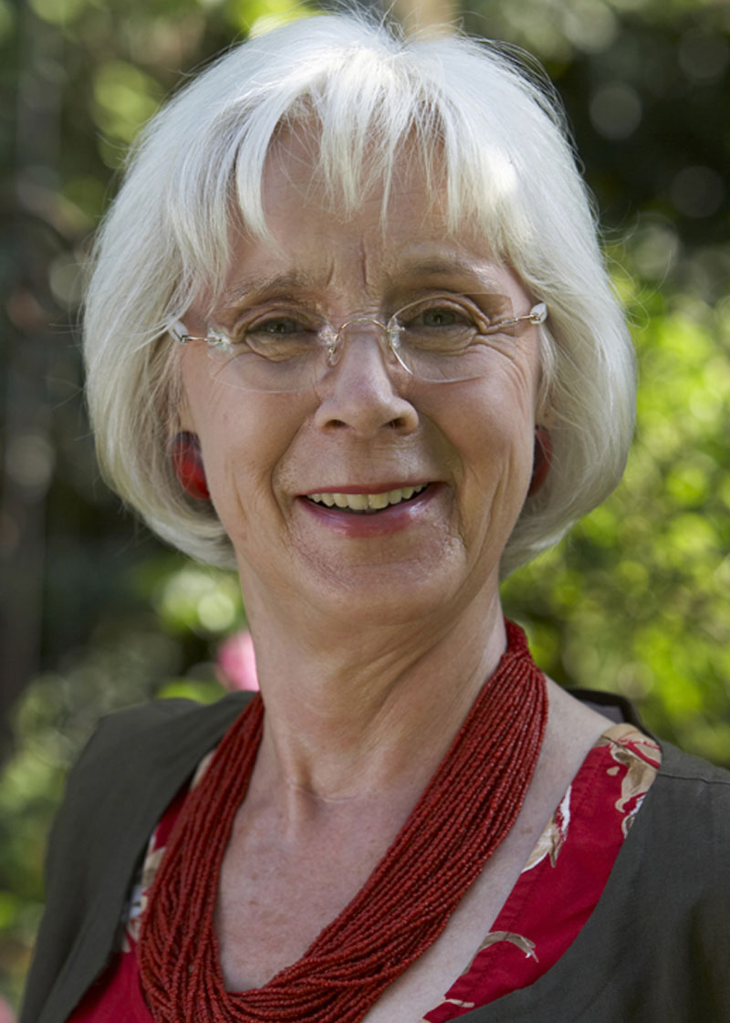 Porträt einer lächelnden Frau mit weißem Haar im Freien.