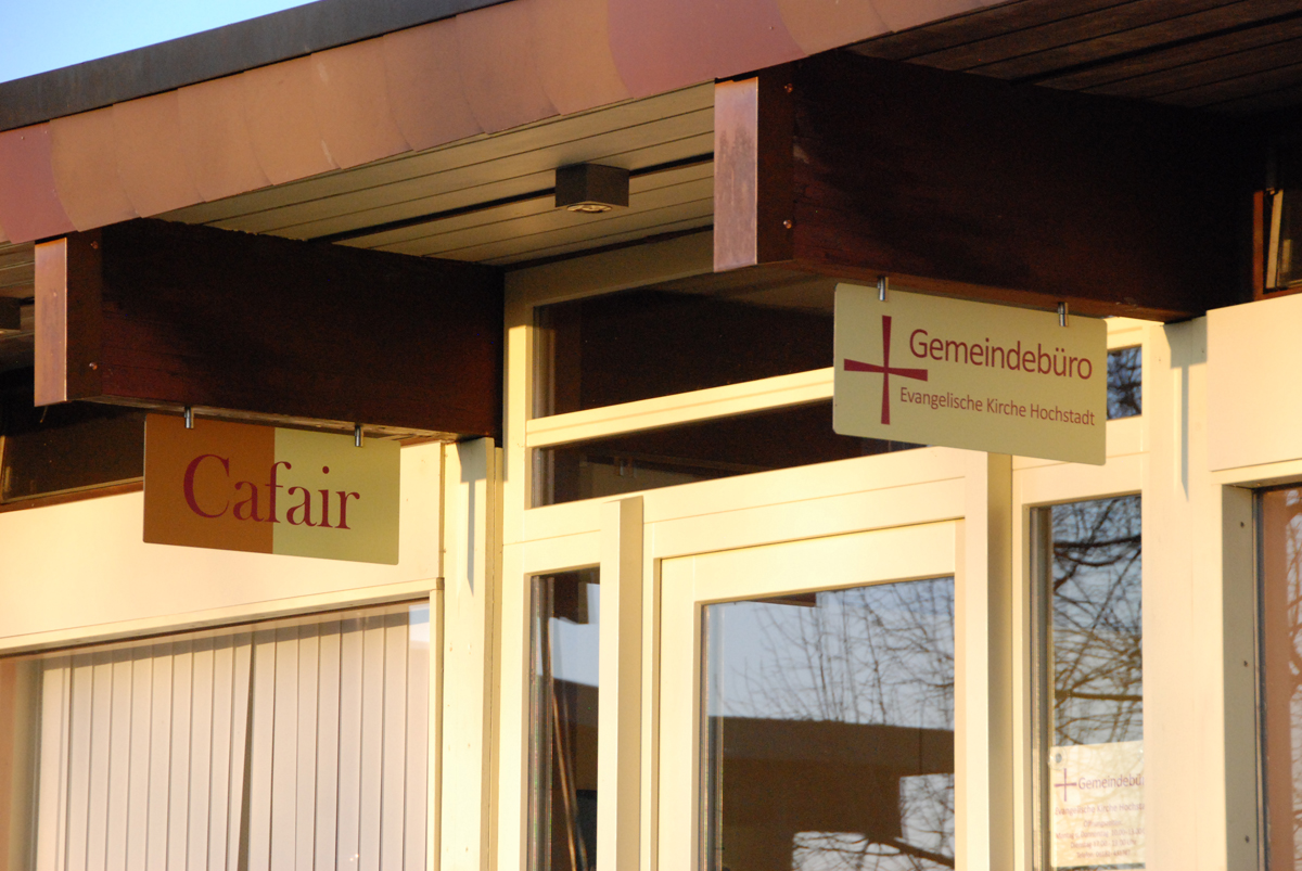 Schilder für "Cafair" und "Gemeindebüro" am Kirchengebäude.