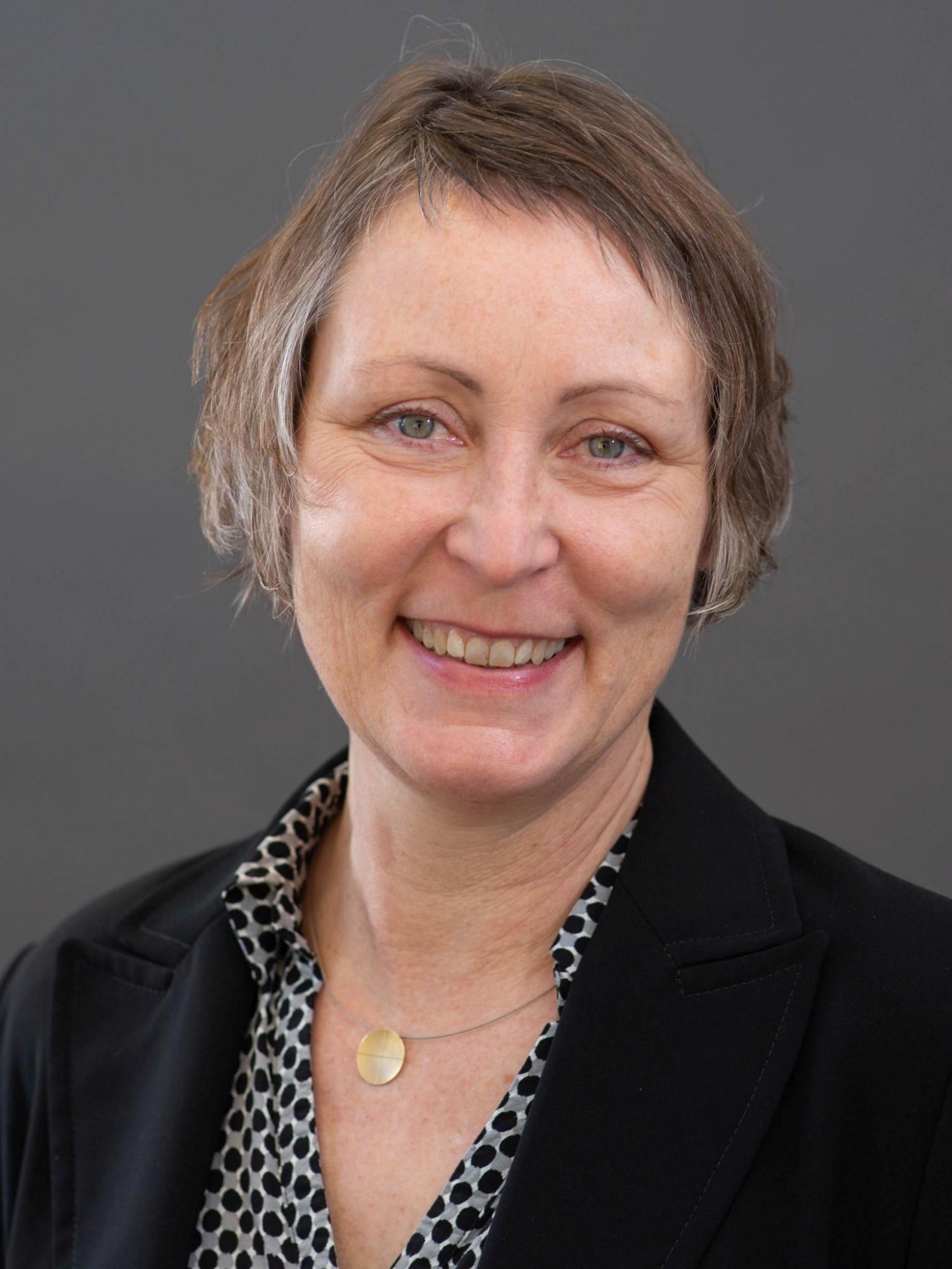 Professionelles Porträt einer lächelnden Frau mit kurzen Haaren.