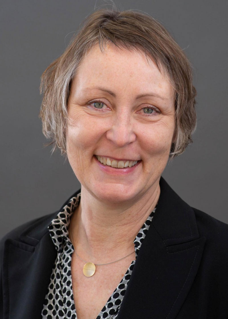 Professionelles Porträt einer lächelnden Frau mit kurzem braunem Haar.