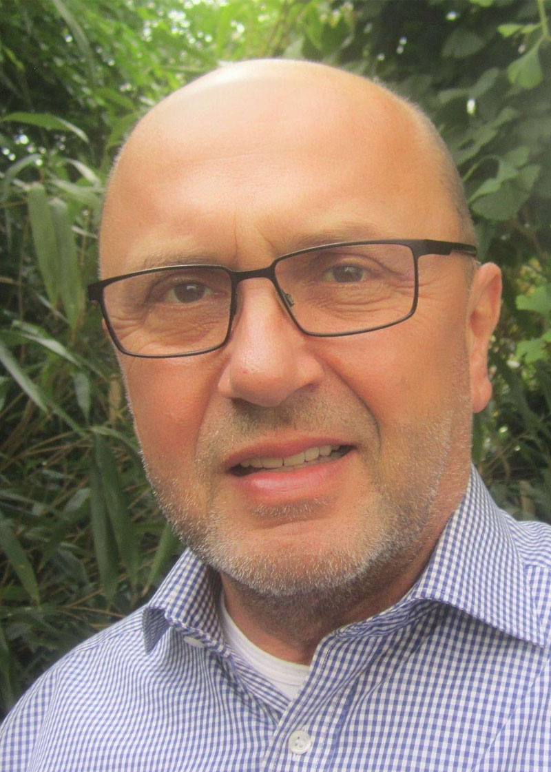 Porträt eines glatzköpfigen Mannes mit Bart und Brille im Freien.